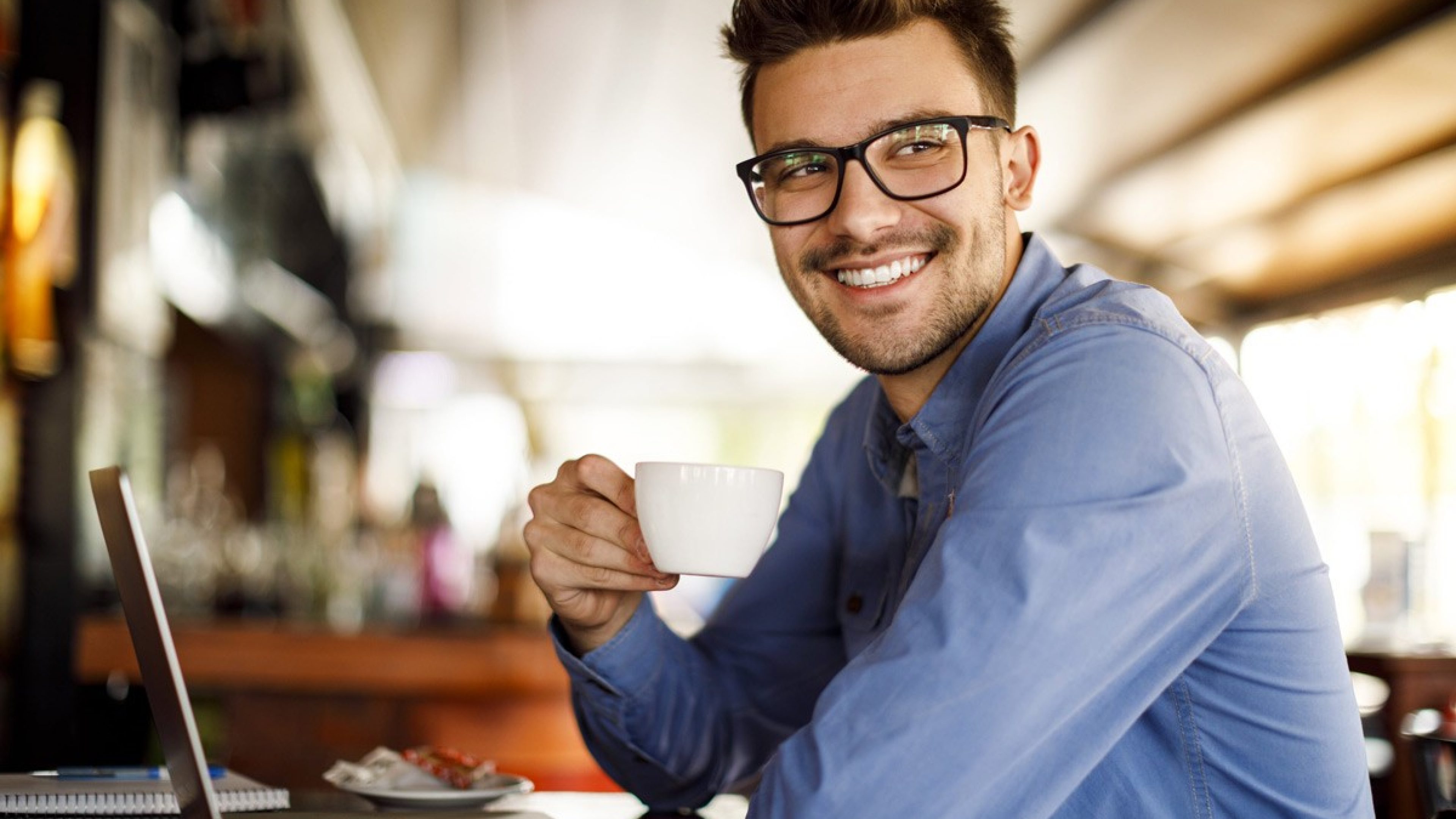 Mann mit Kaffeetasse sitzt in einem Café vor seinem Laptop