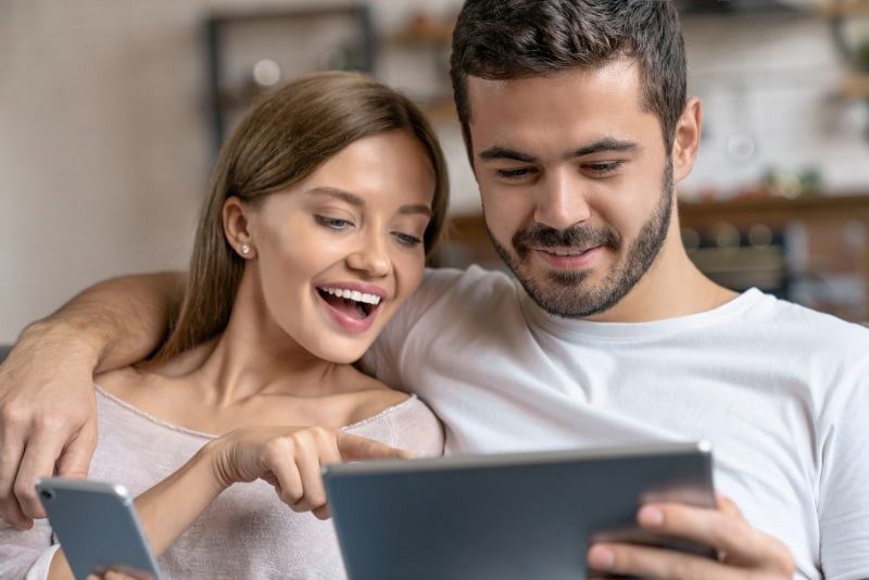 Mann legt Freundin den Arm um die Schultern und beide schauen auf ein Tablet