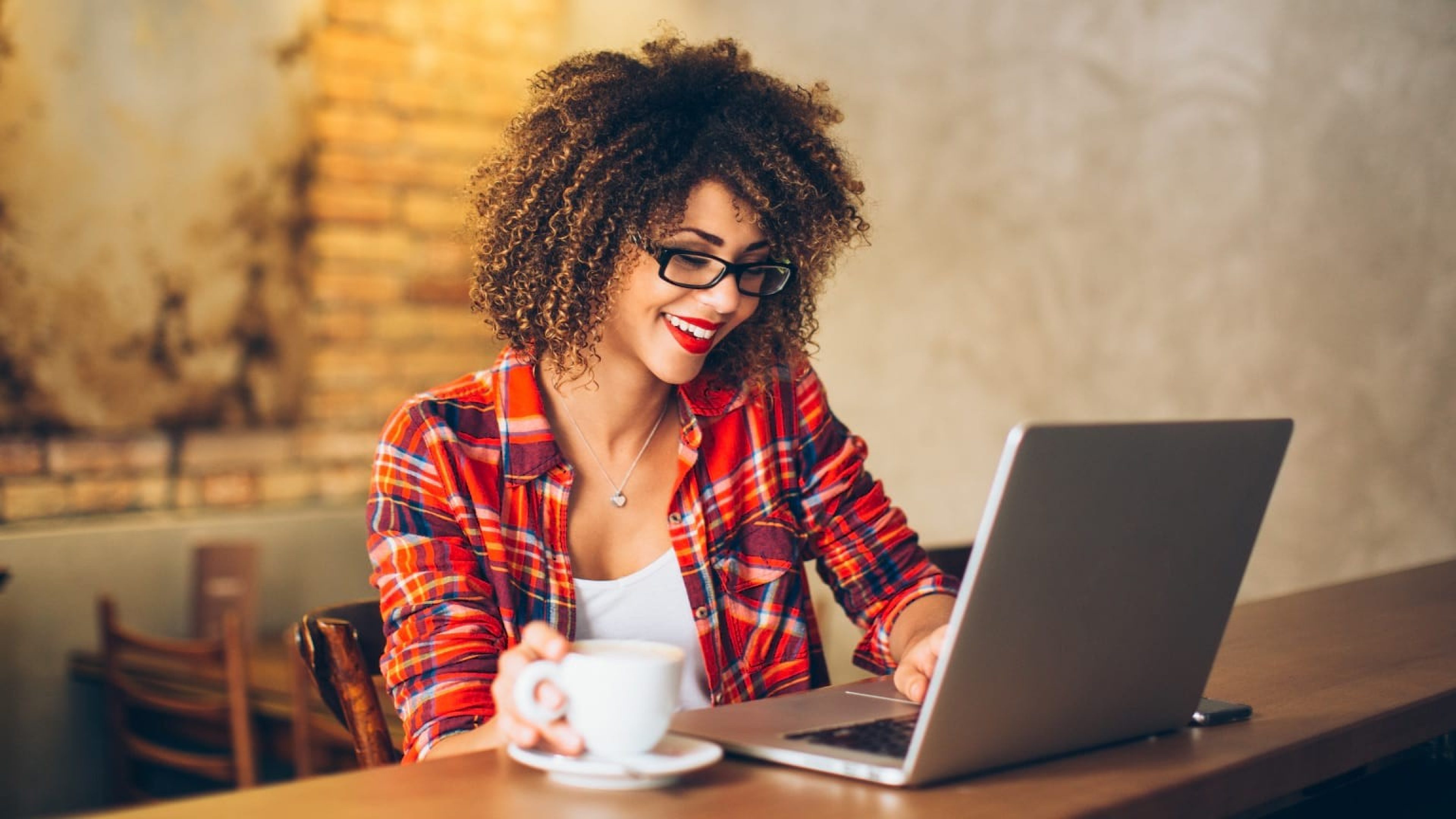 Junge Frau sitzt mit einer Tasse Kaffee vor Laptop 